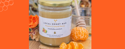 Jar of Vitamin C infused local honey from the Local Honey Man with fresh citrus fruits and floral accents.